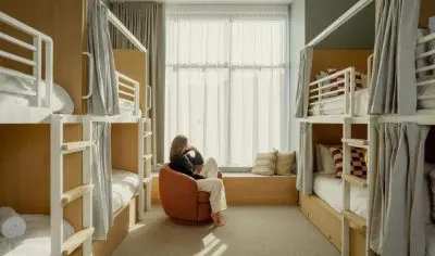 Image of Woman sat chilling in 8 bed female only dorm room where the room is clean and there are privacy curtains for each bunk bed