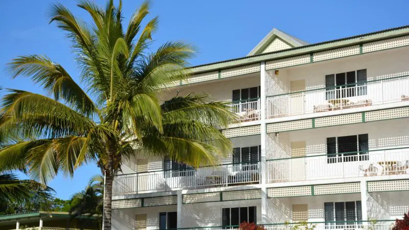 Three-storey accommodation with balconies and palm tree, ideal for your Kgari 4 Day Experience, showcased under vibrant blue skies.