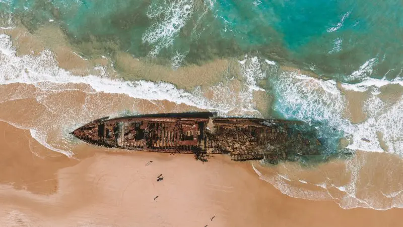 Stunning aerial shot of a rusted shipwreck on pristine sandy beach, ocean waves lapping—ideal for Kgari 3 Day Getaway adventure.