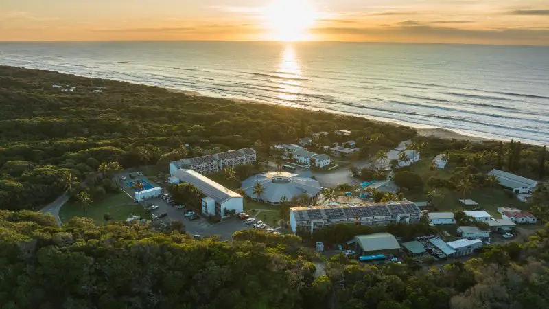 Stunning aerial view of Kgari coastal resort at sunset, perfect for a 3-day getaway, with shimmering ocean waves in the background.