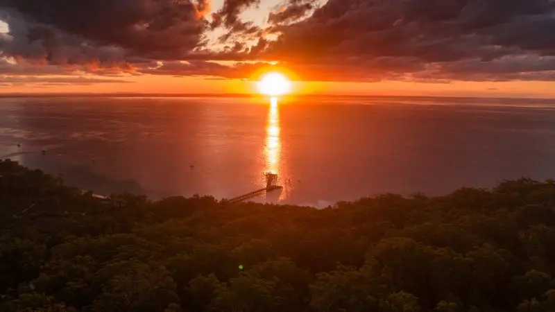 Stunning sunset illuminates the Kgari 5 Day Ultimate pier extending from lush forest to tranquil sea, perfect travel destination.