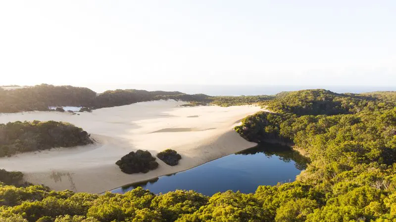 Stunning aerial view of pristine sandy dunes beside a crystal-clear blue lake—ideal for K'gari 3 Day Getaway Illumina adventure.