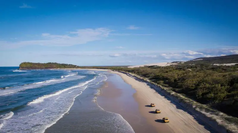 Aerial view of Fraser Island 4WD camping tour vehicles driving along scenic sandy beach, Island Expeditions K'gari Tours adventure.