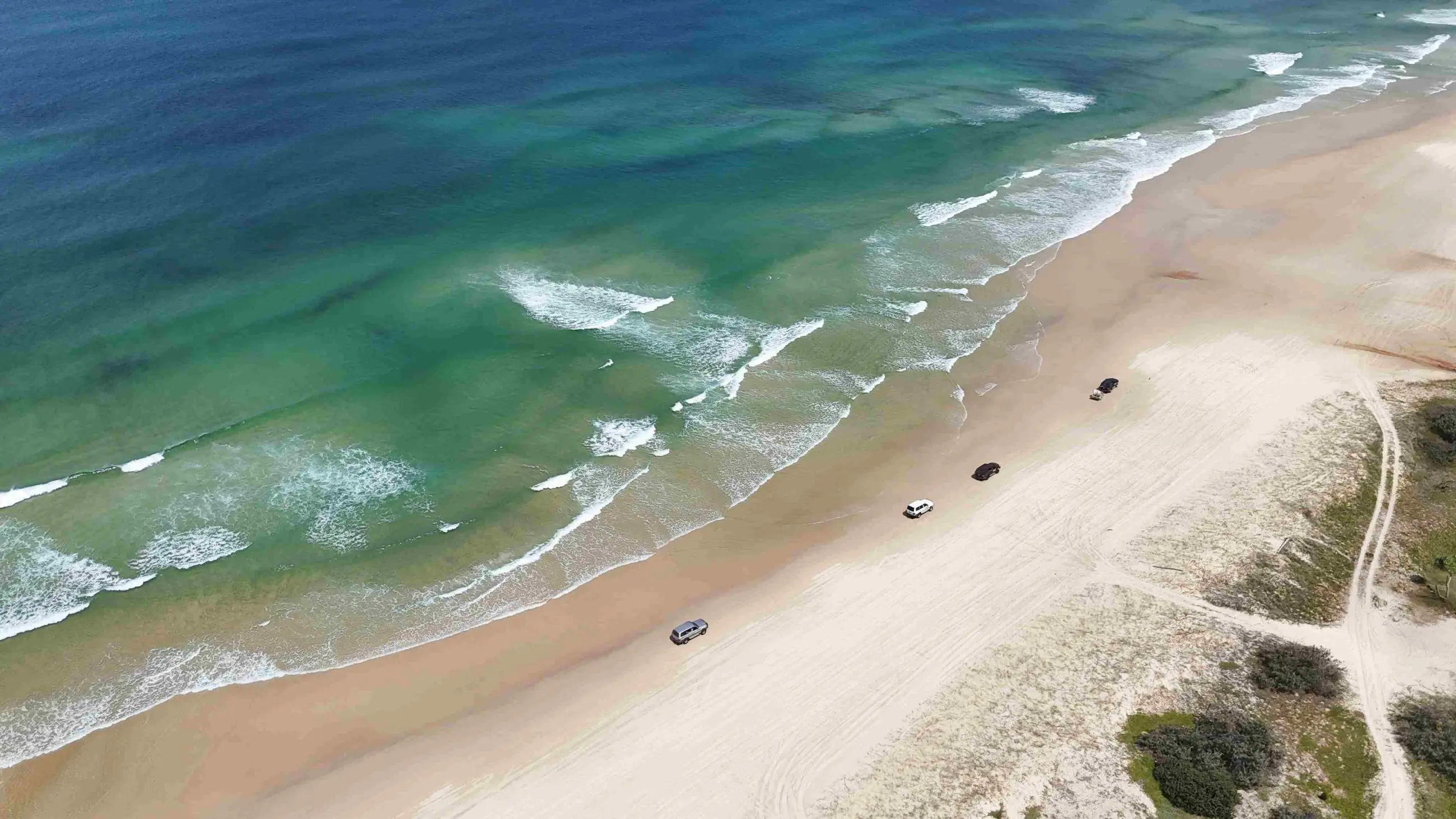 Aerial view of 4WD vehicles driving along pristine sandy beach—perfect for Fraser Island Tag Along Tours from Noosa or Rainbow Beach.