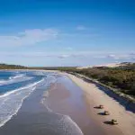 Drone shot of three bright yellow 4WDs driving along Fraser Island beach on K'gari Swag Adventures Tag Along Tour, Australia.
