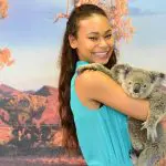 Happy woman in a blue dress holds a koala at Kuranda Koala Gardens, showcasing her 1 Day Kuranda Wildlife Experience Pass.