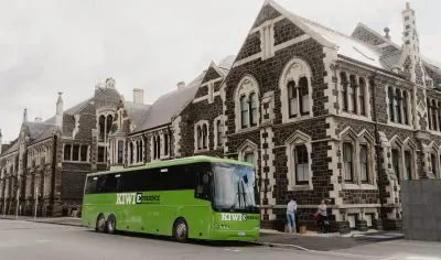 Vibrant green bus parked roadside beside a historic stone building, ideal urban transport near architecture, city street scene.
