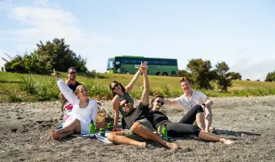 A group of friends relaxing on a sandy beach, surrounded by beach gear, cool boxes, umbrellas, and essentials for the perfect summer day.