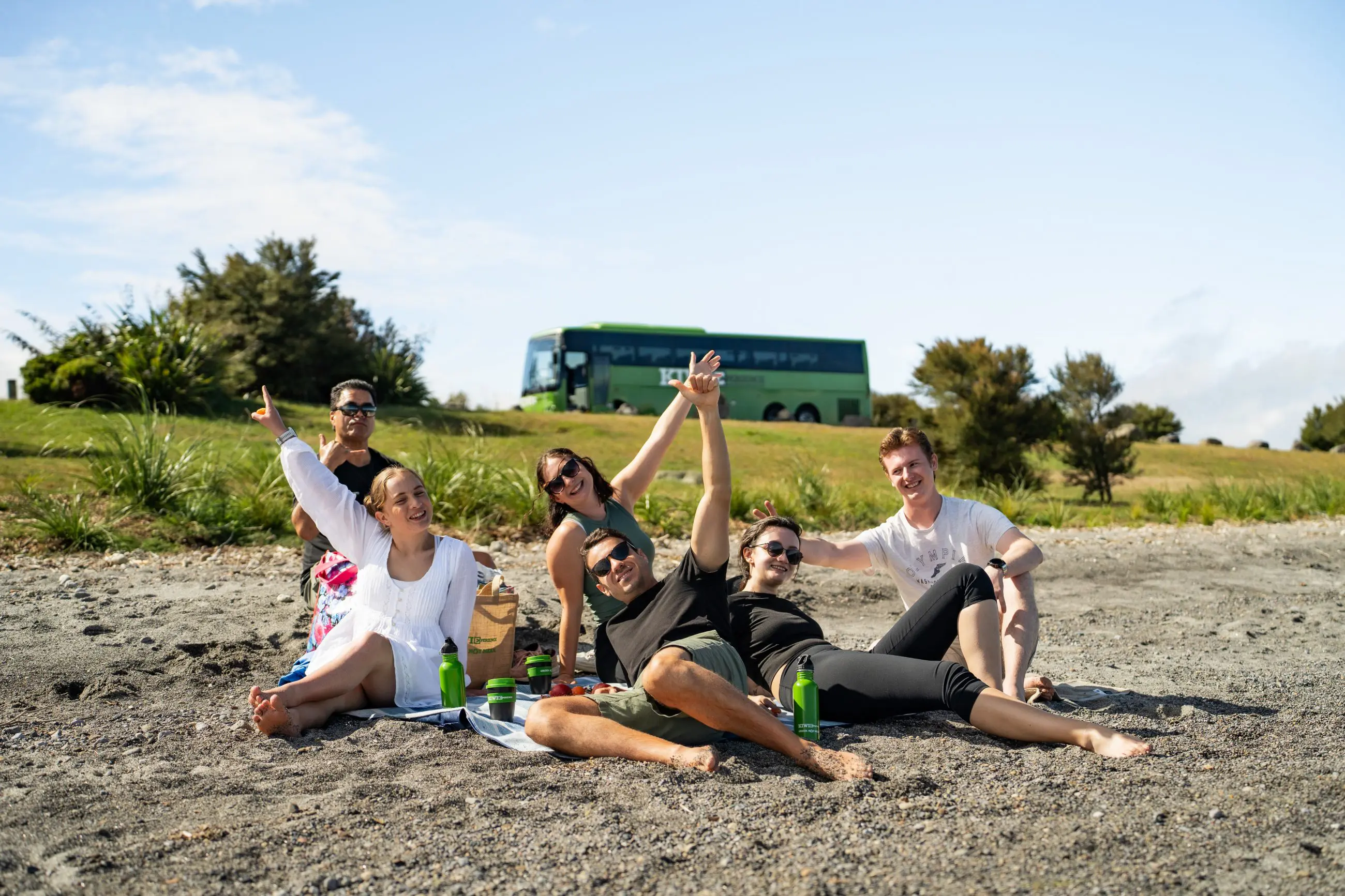 A group of friends relax and enjoy a classic New Zealand beach day, sitting together on golden sand under the sun by the sea.