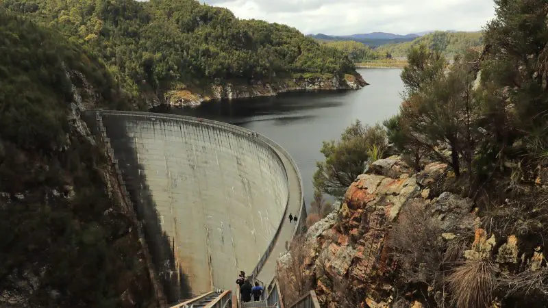 Visitors descend stairs towards the iconic Gordon Dam in Lake Pedder Wilderness on a guided small group tour beneath overcast skies.