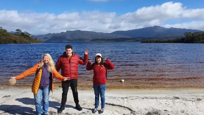 Smiling group of three in jackets at Gordon Dam, enjoying Lake Pedder Wilderness Small Group Day Tour on scenic lakeshore.
