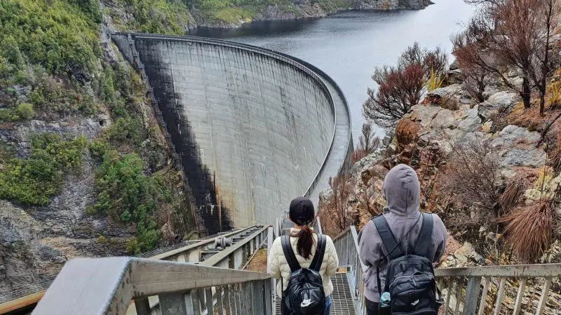 Adventurers with rucksacks hike down stairs towards Gordon Dam in Lake Pedder Wilderness during a guided small group day tour in Tasmania.