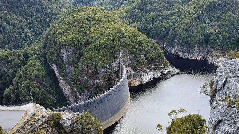 The impressive curved Gordon Dam stretches across tranquil waters, surrounded by lush forested hills on the Lake Pedder Wilderness tour.