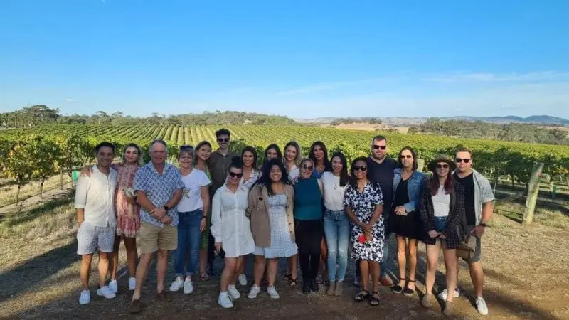 Guests gather in front of lush Barossa vineyards during the Taste The Barossa Premium Wine Tour under a vibrant, sunny blue sky.
