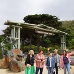 Five women smiling and waving at the iconic Great Ocean Road Memorial Arch during a 4-day, 3-night Great Ocean Road and Beyond tour.
