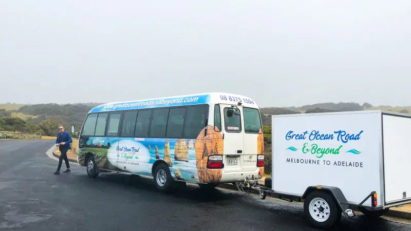 Great Ocean Road and Beyond 4 Day 3 Night Tour coach and trailer parked, branding visible, man standing beside for travel adventure.