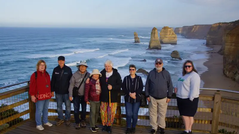 Group of eight on a wooden lookout, stunning ocean cliffs behind, during Great Ocean Road and Beyond 4 Day 3 Night Tour adventure.