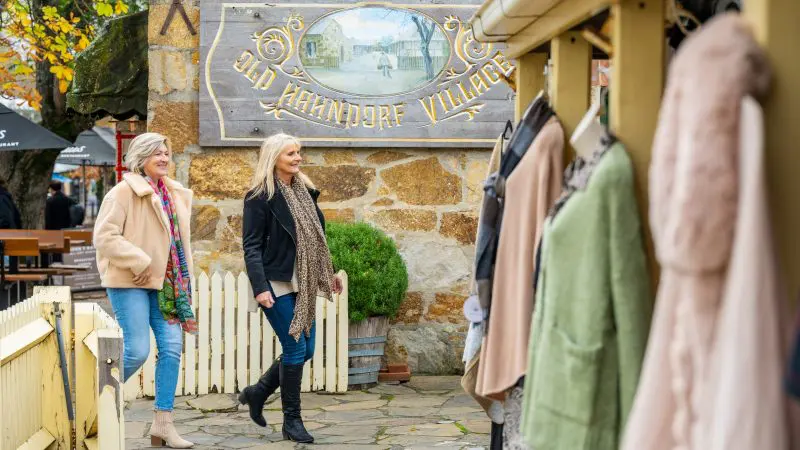 Two women walk by a charming boutique in Old Hahndorf Village during the Adelaide Highlights Wine Tasting Coast Full Day tour experience.