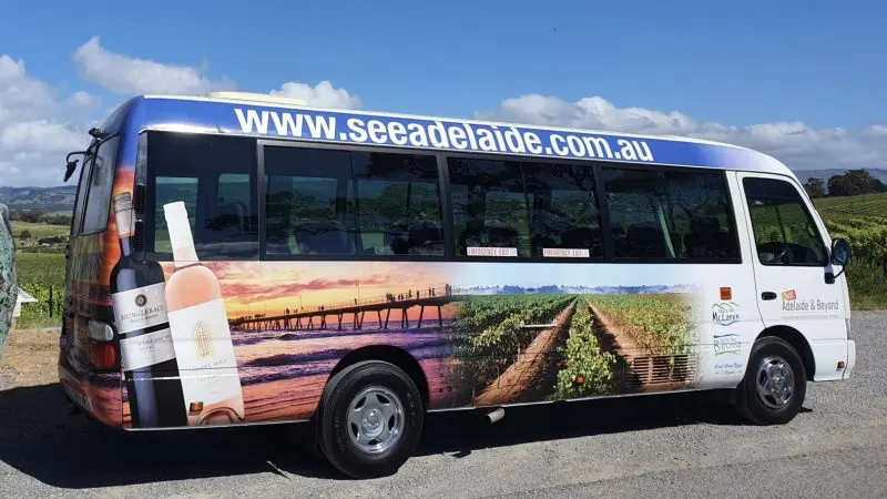 Half-Day Wine Tasting Coast Afternoon Tour coach featuring vineyard imagery, parked by lush vines, branded www.seeadelaide.com.au.