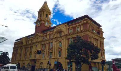 Iconic historic yellow clocktower building in Auckland at a busy street corner, ideal for city sightseeing under partly cloudy skies.