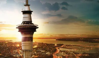 Auckland Sky Tower at sunset with city lights sparkling over the harbour—ideal for private tours or immersive Māori cultural experiences.