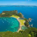 Stunning aerial view of Bay of Islands, featuring vibrant lush greenery, sailboats on crystal-clear turquoise waters, and pristine sandy beach.