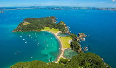 Stunning aerial view of Bay of Islands, featuring vibrant lush greenery, sailboats on crystal-clear turquoise waters, and pristine sandy beach.