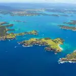Stunning aerial view of Bay of Islands’ lush green islands and turquoise waters, boats cruising near the iconic Hole in the Rock.