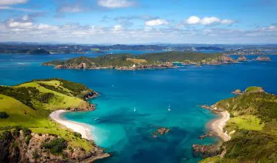 Stunning aerial view of Bay of Islands with turquoise waters, lush green islands, and a vibrant blue sky dotted with fluffy white clouds.