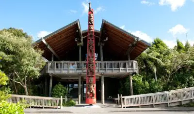 West Coast building with wooden roof and balcony beside a striking tall red totem pole, ideal for regional cultural discovery holidays.