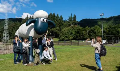 A smiling group poses next to a giant Shaun the Sheep statue in a sunny Rotorua park, capturing top New Zealand holiday moments.