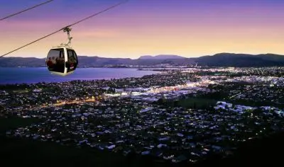 Experience breathtaking dusk views as a cable car soars over Rotorua, revealing a glowing lake and mountains beneath a radiant purple sky.