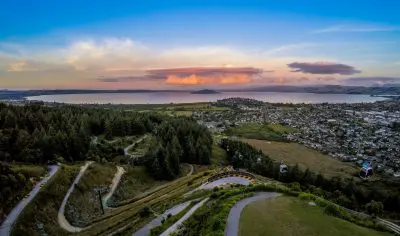 Breathtaking aerial view of Rotorua at sunset, surrounded by lush forests, winding roads, and a serene lake—ideal for adventure seekers.