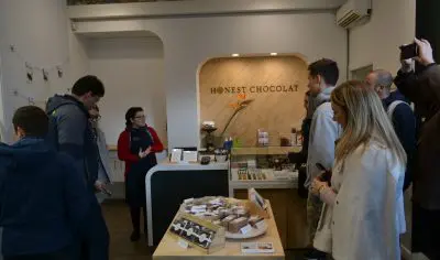Matakana wine tour group attentively listens to Honest Chocolate shop staff, exploring gourmet chocolate and wine tasting experience.