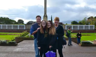 Happy family of four posing outdoors in Auckland City near a prominent monument under an overcast sky, capturing joyful memories.