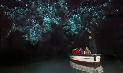 Visitors marvel at the vibrant blue glow illuminating the ceiling of New Zealand’s famed Waitomo Glow Worm Caves in darkness.