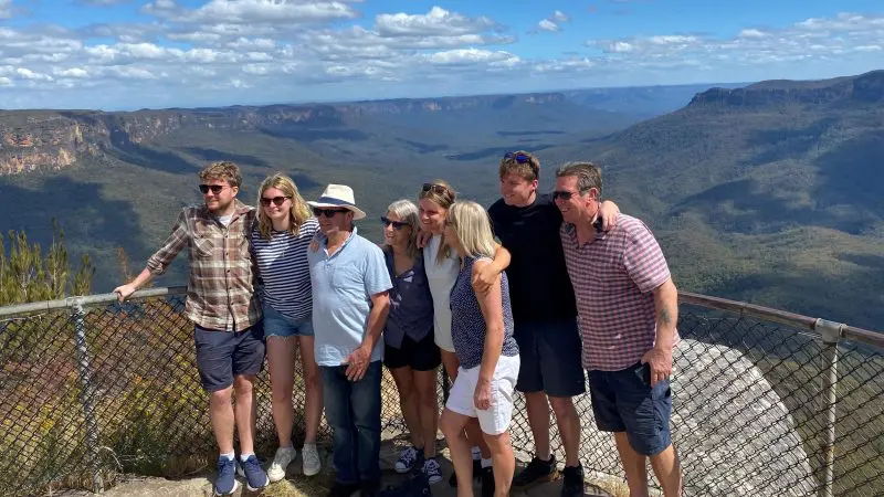 Group of seven enjoying panoramic Blue Mountains lookout on a 1 Day Sunset Wilderness Tour, dramatic clouds overhead, scenic views.
