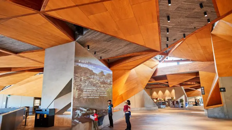 Modern museum interior featuring a wooden ceiling, concrete pillars, and an exhibition on 1 Day Phillip Island Penguin Parade and koalas.