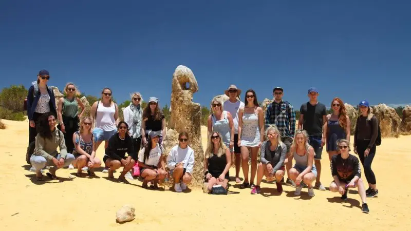 Tour group enjoys the Pinnacles Desert at sunset on a 1 Day Stargazing Tour with Autopia, beneath a vibrant, cloudless blue sky.