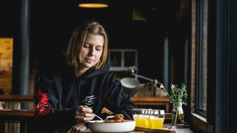 A guest in a black jumper savours lunch by a sunlit window after an unforgettable Huon Valley Safaris Private Day Tour experience.