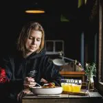 Traveller enjoys fresh meal by a sunny window on Huon Valley Safaris Private Day Tour, with juice and flowers elegantly set on table.