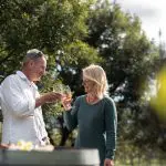 Joyful couple toasting wine glasses on the Tasman Safaris Port Arthur Harbour Cruise and Lunch Private Day Tour, outdoor setting.