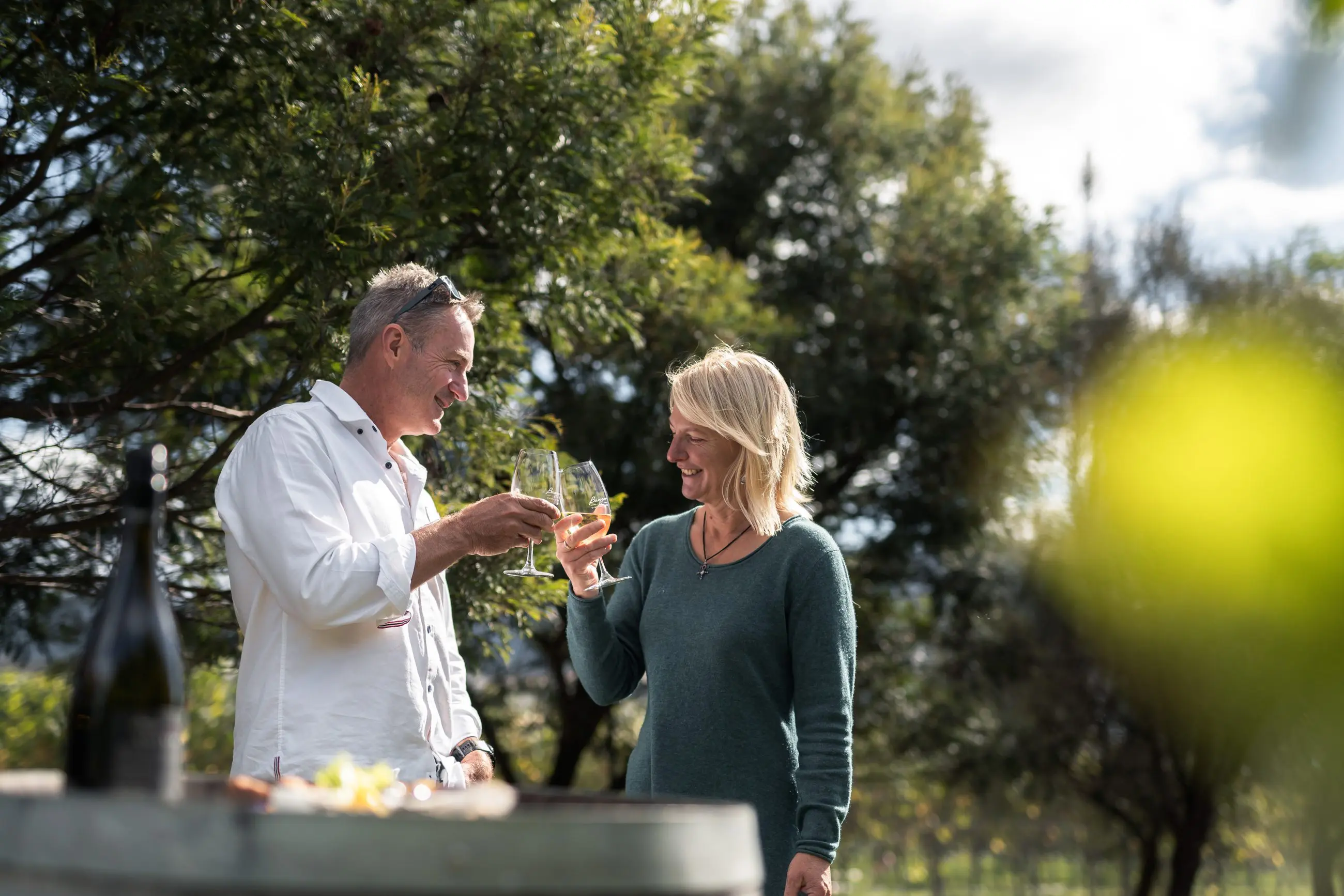 Joyful couple toasting wine glasses on the Tasman Safaris Port Arthur Harbour Cruise and Lunch Private Day Tour, outdoor setting.