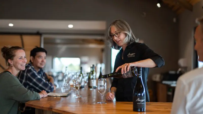 A woman expertly pours wine for guests at a sleek wooden bar in a modern tasting room on a Tasman Safaris Port Arthur tour.