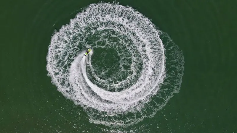 A jet ski carves swirling white waves on vibrant green water, forming a striking spiral pattern reminiscent of Die Another Day.