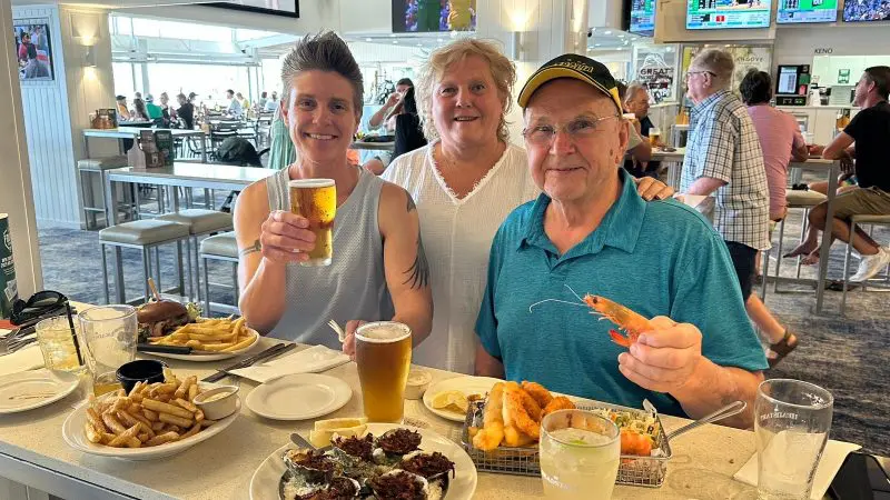 Three friends laughing whilst dining at a restaurant, savouring fresh seafood and drinks on the G'day Be An Aussie For A Day Tour.