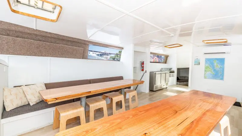 Luxurious, contemporary Summer Jo yacht interior featuring sleek wood tables, elegant stools, plush bench seating, and modern galley.