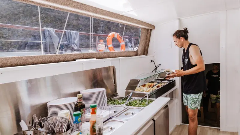 A guest serves fresh buffet food including salad, plates, and condiments aboard the Summer Jo Day Charter boat’s dining area.