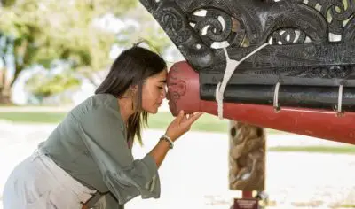 Woman engaging in a traditional hongi greeting with a carved Māori figure at New Zealand’s historic Waitangi Treaty Grounds.