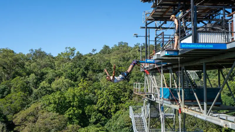 Thrill-seeker bungee jumps at Australia’s only bungy Skypark, framed by vibrant green forest and a crystal-clear blue sky above.